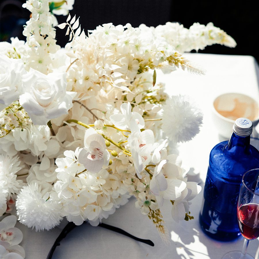 Weißes Blumengesteck mit blauen Gläsern auf dem Tisch